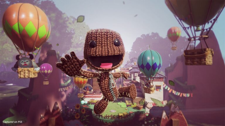 Sackboy springt auf die Spielenden zu. Im Hintergrund ist ein kleines Dorf um das viele Heißluftballons schweben.