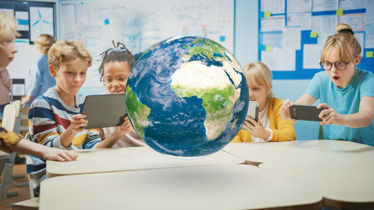 Kinder sitzen mit ihren Tablets um einen Tisch auf dem eine große Weltkugel schwebt.