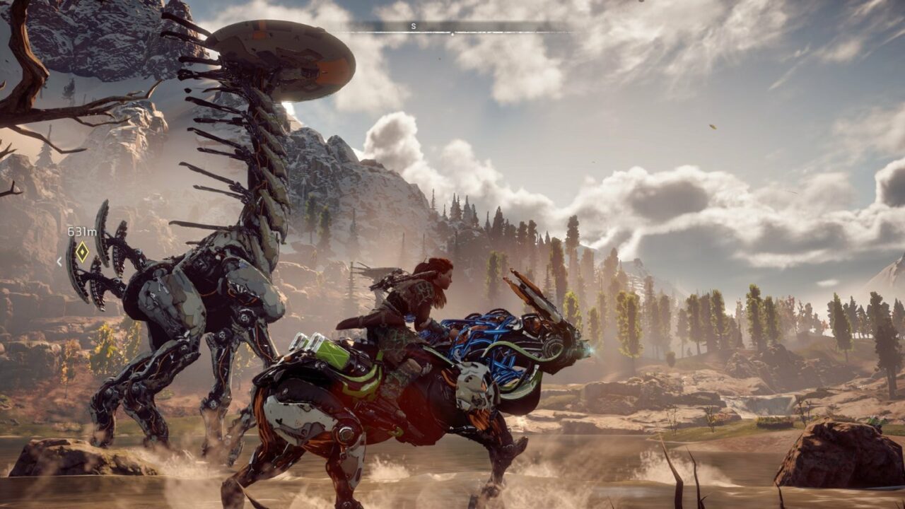 Protagonistin Aloy reitet auf einem Roboter-Tier durch eine karge Landschaft. im Hintergrund ist ein überdimensional großer Roboter Dinosaurier zu sehen.