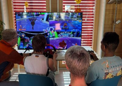 Menschengruppe spielt Mario Kart Acht Deluxe mit Lenkrad und Controller.