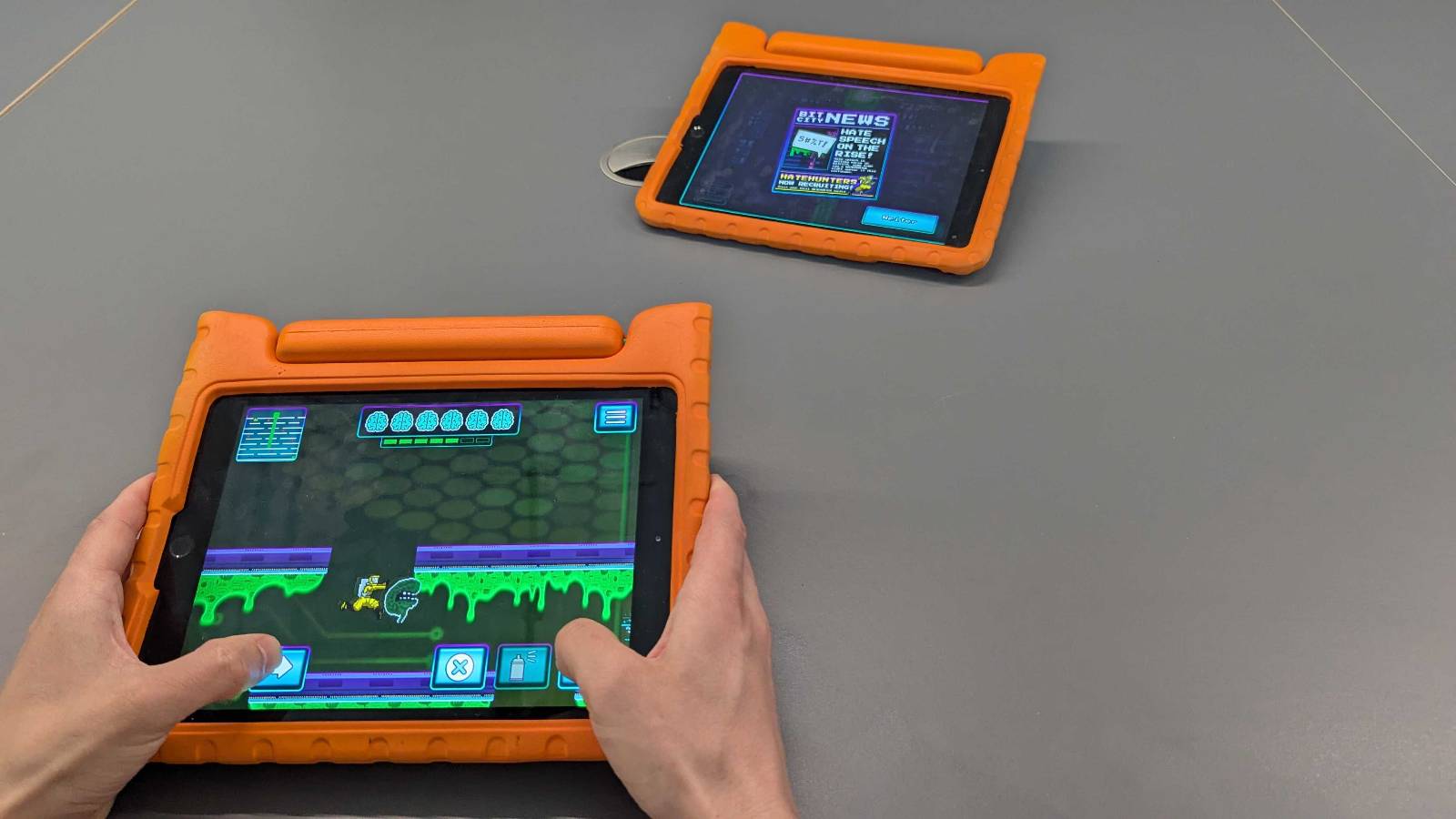Point of View von zwei Händen die ein Tablet halten und darauf ein Plattformer Computerspiel spielen. Ein weiteren Tablet liegt auf einem Tisch.